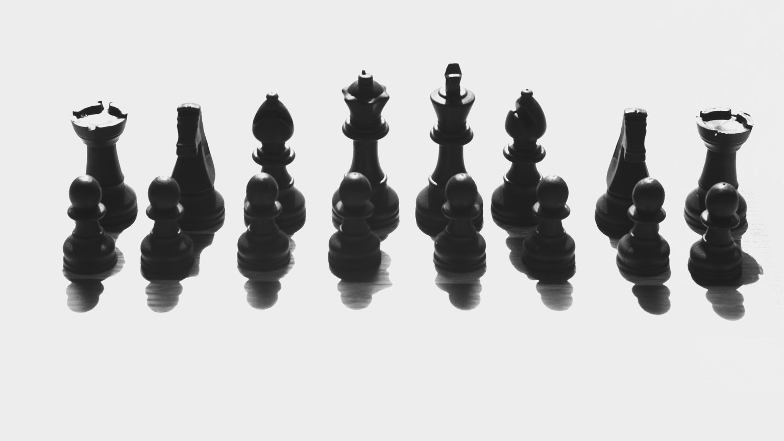 Black chess pieces arranged in a dramatic shadow cast on a white background.