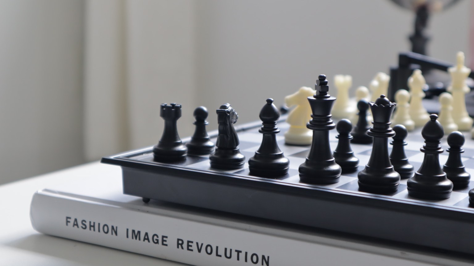Black chess pieces on a board placed atop a fashion book, conveying strategy and style.