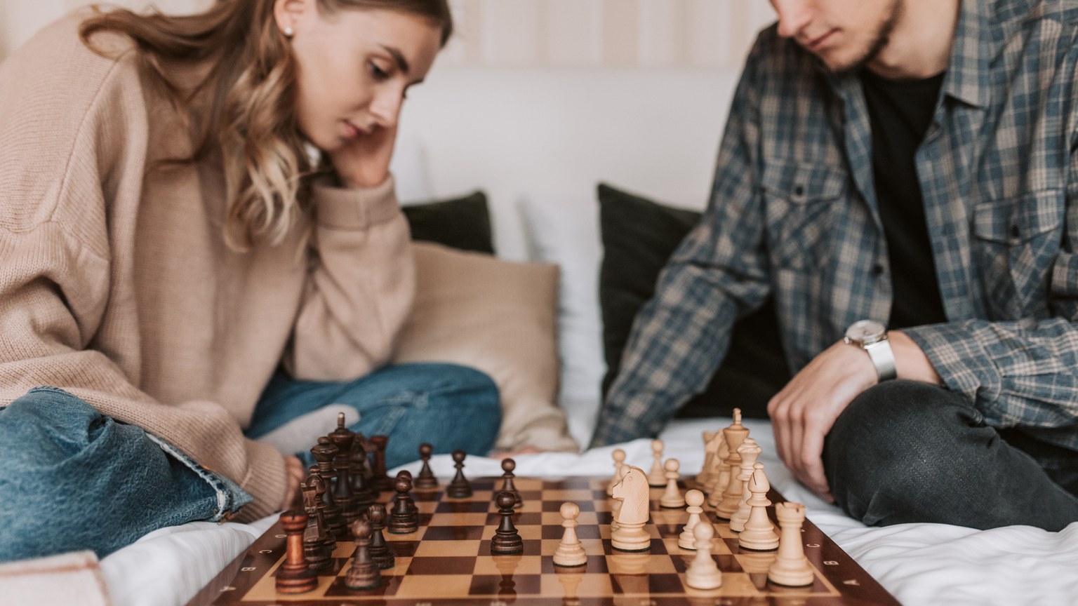 A young couple deeply focused on a chess game in a cozy indoor setting.