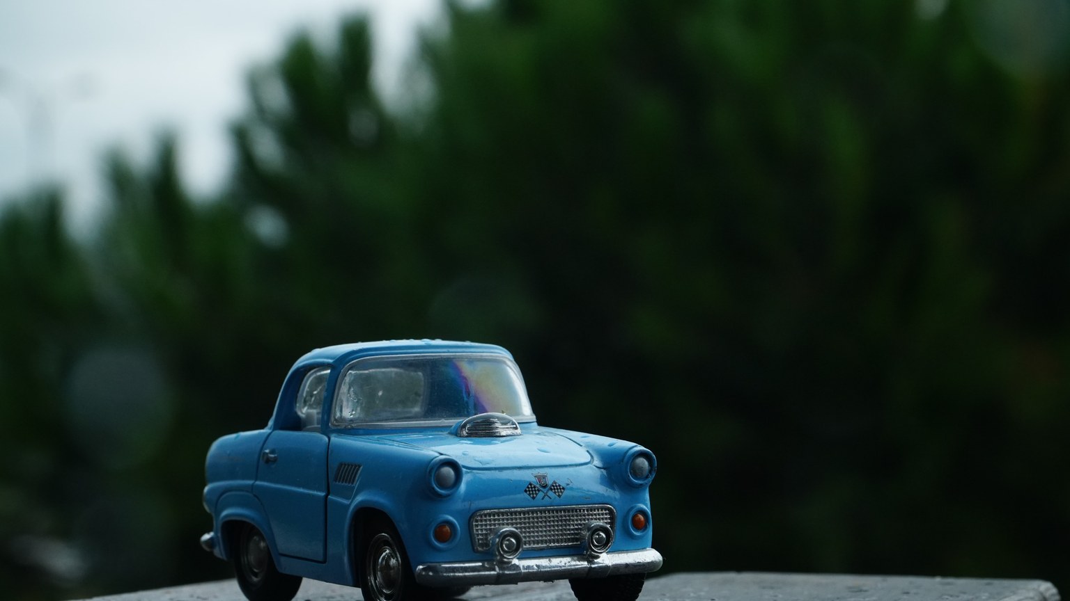 A close-up of a vintage blue toy car on a wet surface with a blurred green background.