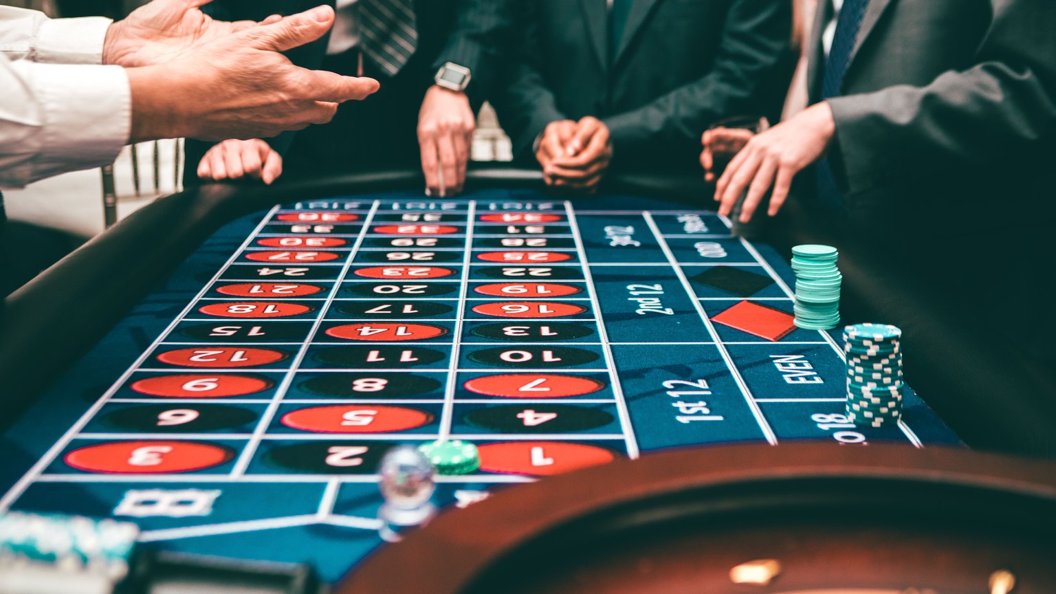 Group of people playing roulette, placing bets in a casino setting.