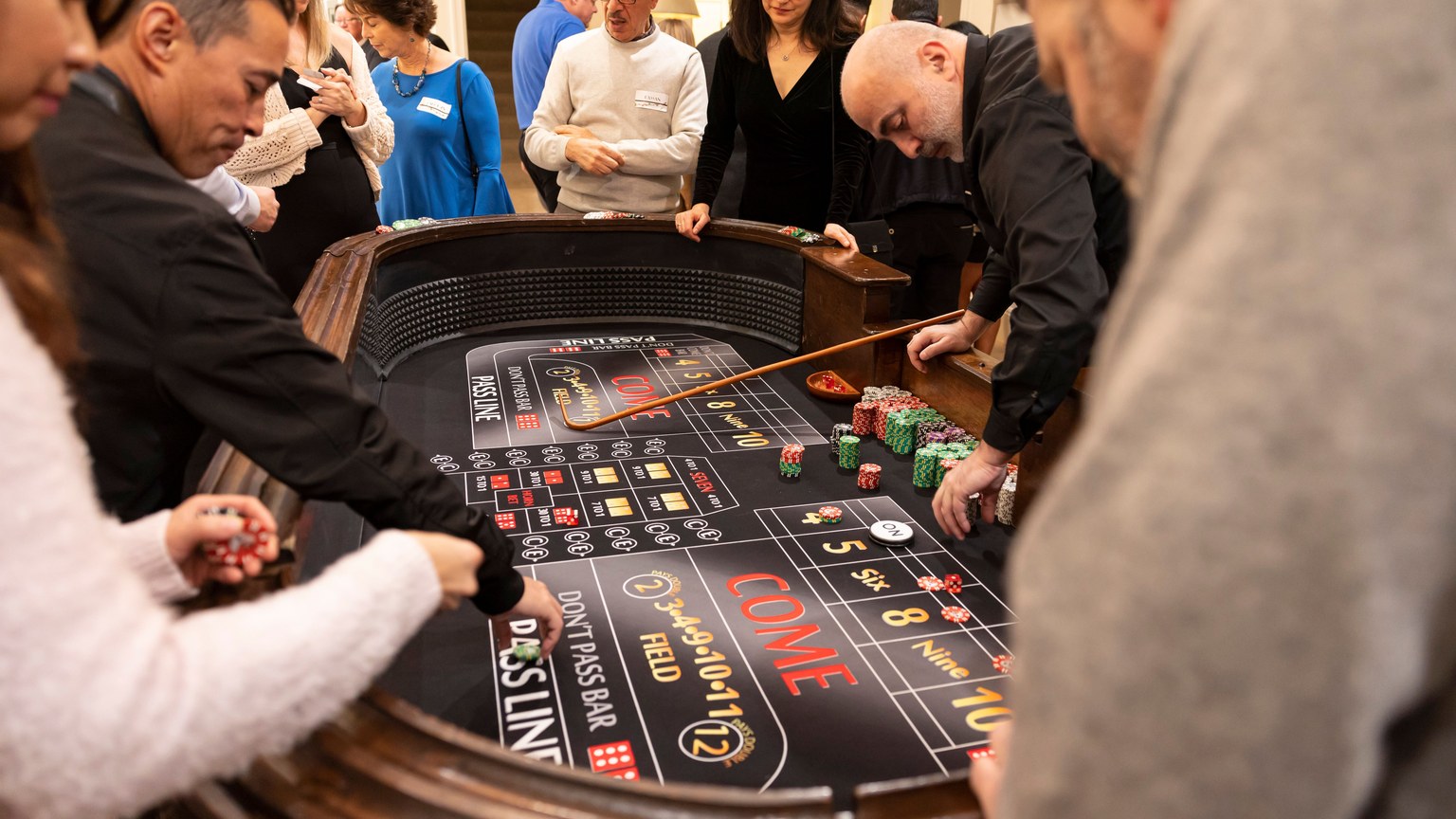 Group of adults playing craps around a casino table, engaging in betting and socializing.