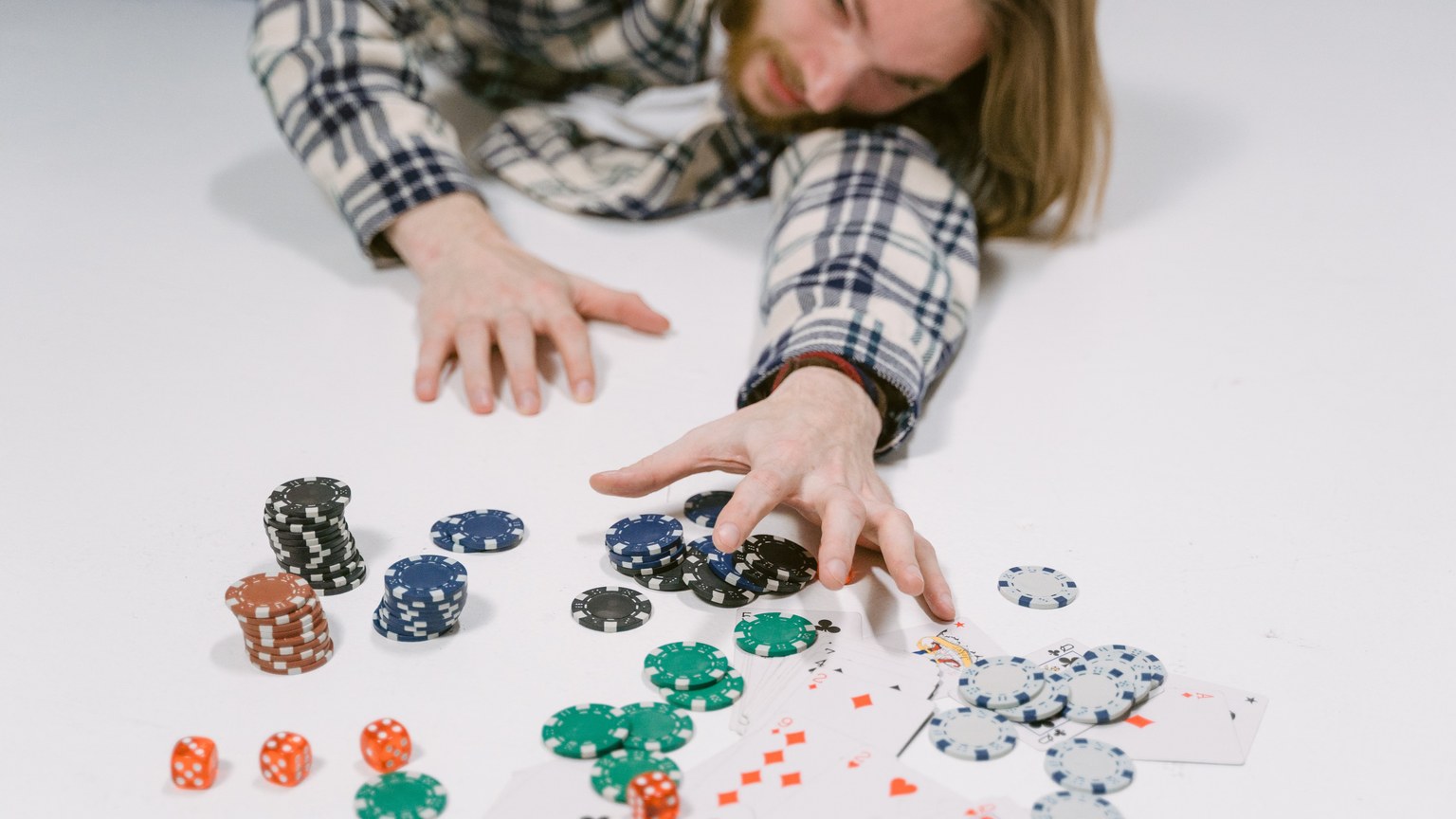 A man in a plaid shirt reaches for poker chips on a white surface, depicting a gambling scene.