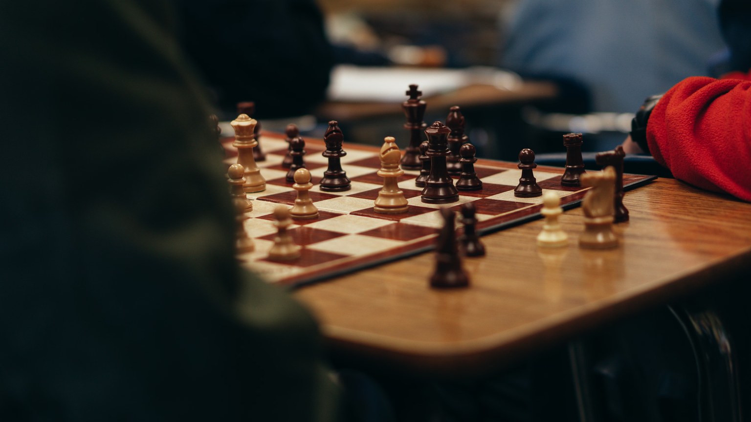 High angle of crop anonymous people sitting at table and playing chess in club