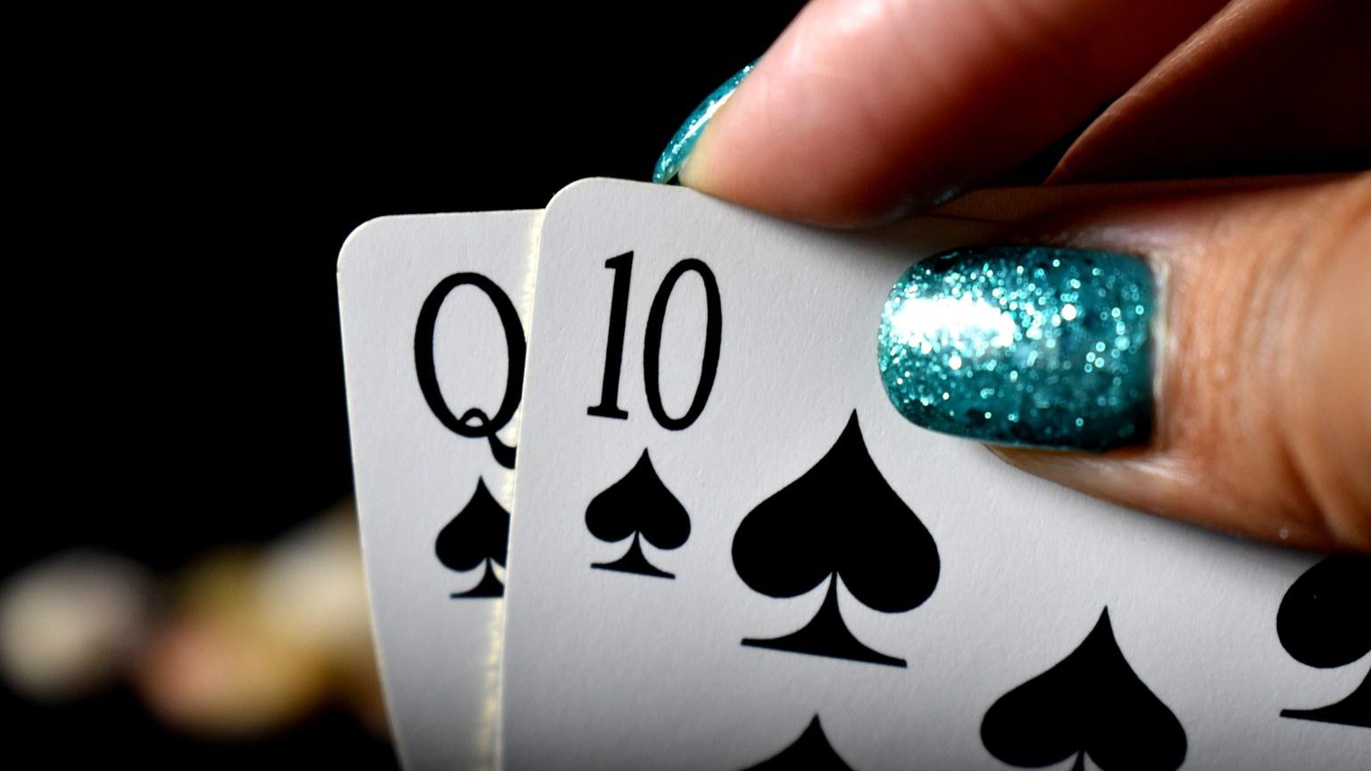 Intense close-up of a hand holding Queen and Ten of spades in a poker game.