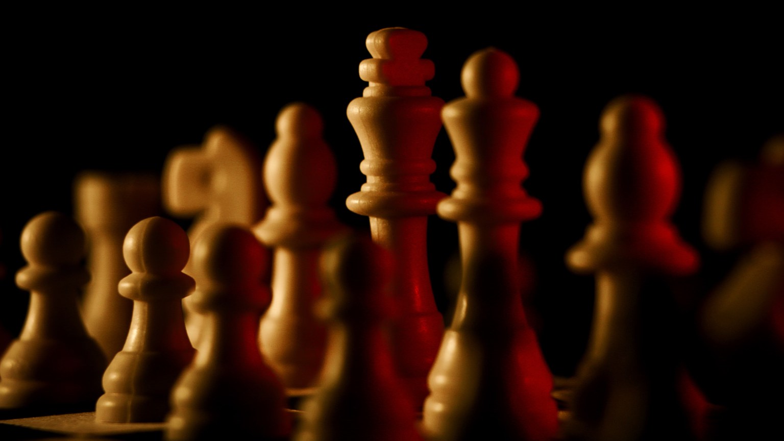 Chess pieces lit dramatically on a black background, evoking strategy and focus.