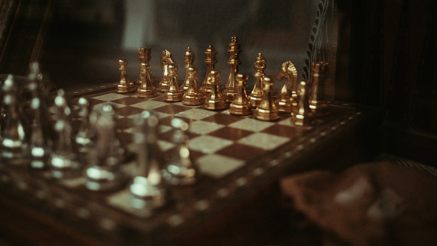 Close-up of a sophisticated chess set with gold and silver pieces on a wooden board.