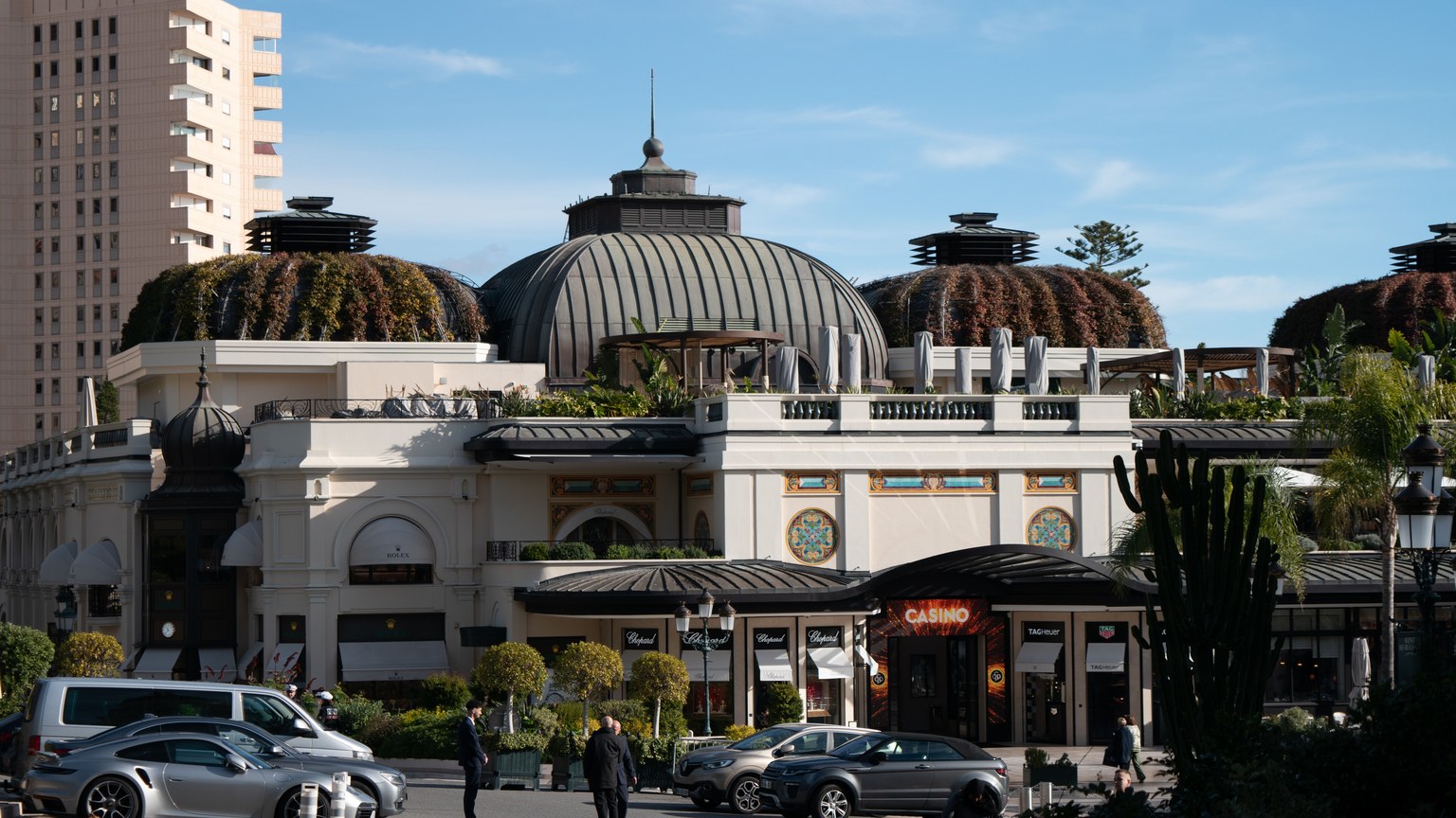 A sunny day view of the architecturally stunning casino in Monaco, featuring elegant domes and lush greenery.