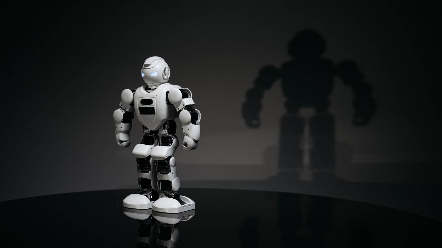 A white and black toy humanoid robot in a studio setting casting a shadow.