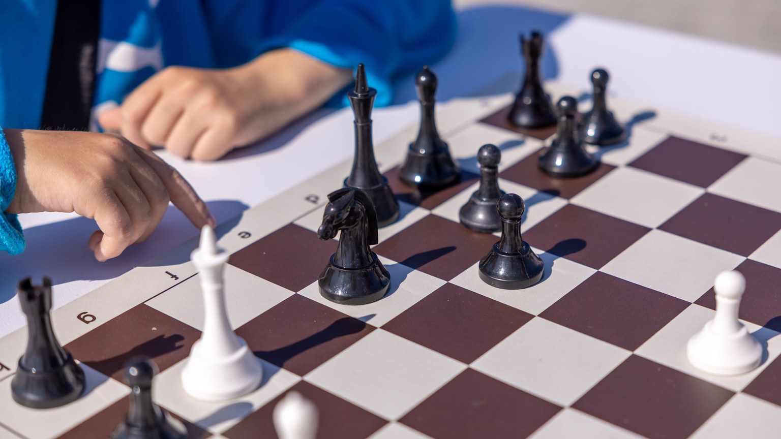 A child plays chess outdoors, focusing on strategy with black and white pieces on a sunny day.