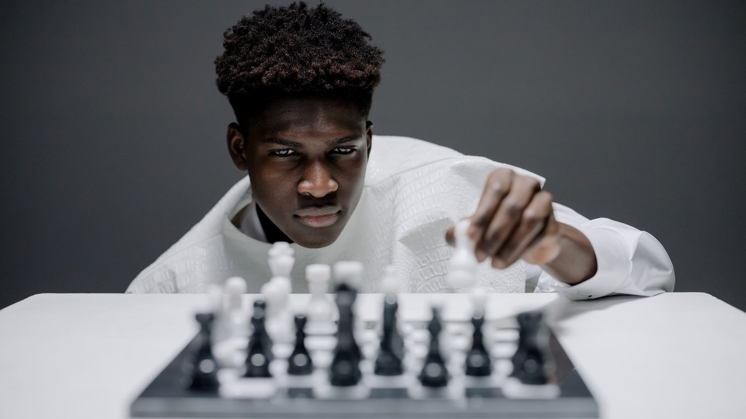 Young man in white playing chess indoors, demonstrating concentration and strategy.