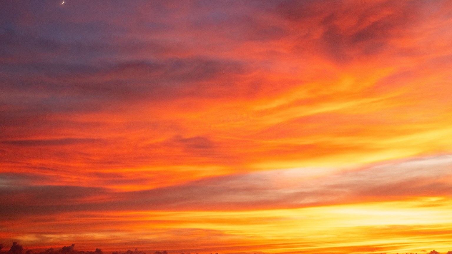 Stunning sunset with a crescent moon, rich orange and red hues create a dramatic sky view.