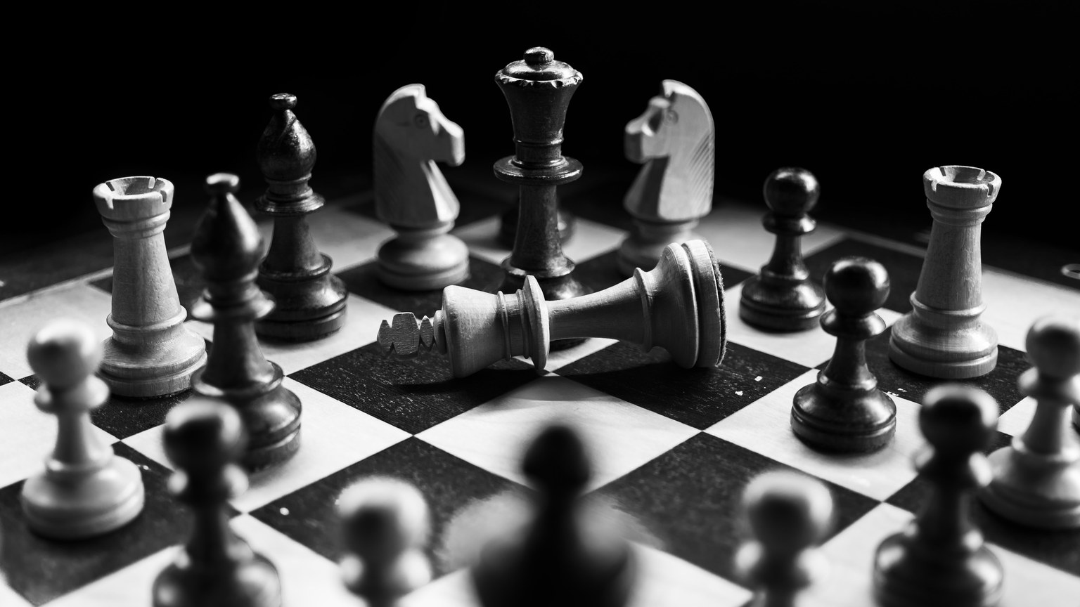 A captivating black and white photo of a chess game with fallen king piece, symbolizing defeat.